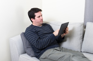 Hombre de mediana edad tumbado en un sofá utilizando una tablet.